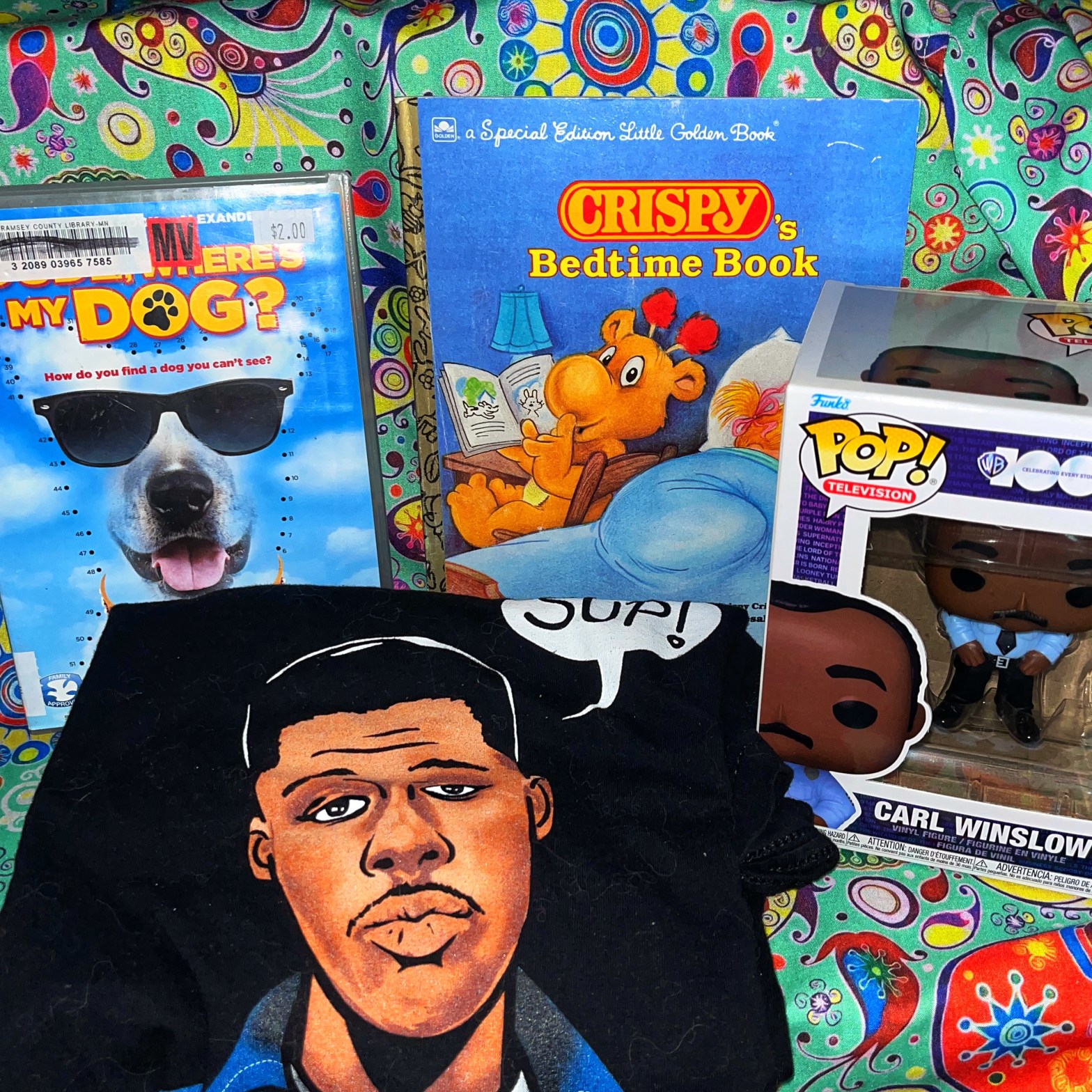 A DVD of Dude Where's My Dog. The children's book Crispy's Bedtime Book. A shirt with Waldo Geraldo Faldo saying "Sup?". And the Pop figure of Carl Winslow.